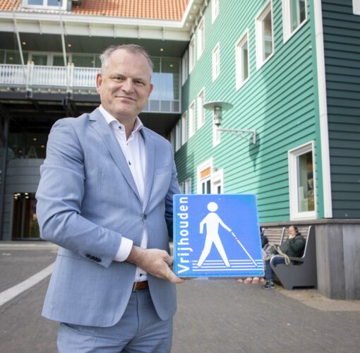 Afbeelding De wethouder van de gemeente Zaanstad houdt de permanente stoeptegel "Houd de lijn vrij" omhoog, staande op straat in zijn gemeente