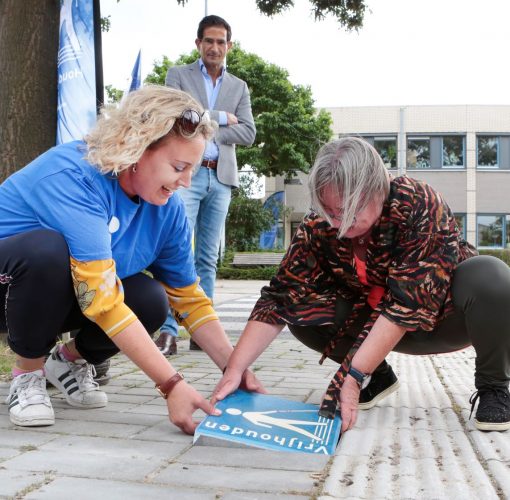 Afbeelding Een cliënt en medewerker van Visio leggen de stoeptegel in Huizen